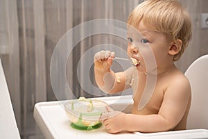 Cute little boy alone eating porridge with a spoon from a plate, healthy eating concept. The kid learns to eat with a spoon on his