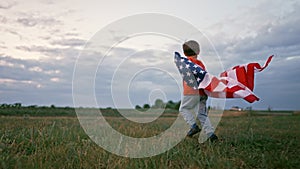 Cute little boy - American patriot kid running with national flag on open area field. USA, 4th of July - Independence
