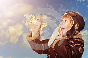 Cute little boy aviator wit wooden plane toy against blue sky background