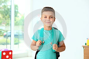 Cute little boy with backpack in classroom
