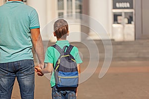 Cute little boy with backpack going to school with his father. Back view.