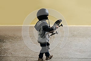 Cute little boy in a black helmet walking away, stepping on concrete floor