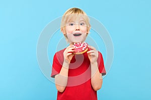 Cute little boy with blond hair and freckles eating a glazed donut. Children and sugary junk food.