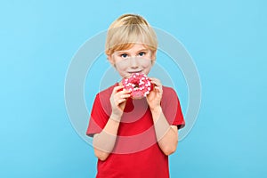 Cute little boy with blond hair and freckles eating a glazed donut. Children and sugary junk food concept.