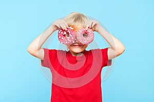 Cute little boy with blond hair and freckles having fun with glazed donuts. Children and sugary junk foods.
