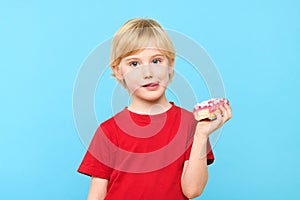 Cute little boy with blond hair and freckles having fun with glazed donuts, sticking tongue out.