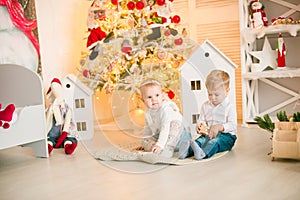 Cute little boy with blond hair plays with little girl in a bright room decorated with Christmas garlands