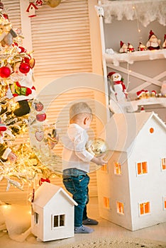 Cute little boy with blond hair plays with  toys in a bright room decorated with Christmas garlands near the Christmas tree.