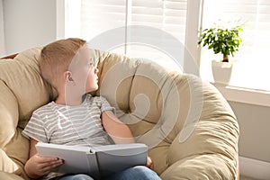 Cute little boy with book in papasan chair