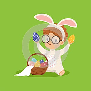 Cute little boy with bunny ears and rabbit costume playing with basket with painted eggs, kid having fun on Easter egg