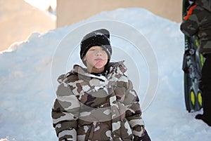 Cute little boy in camo ski jacket eating snow.