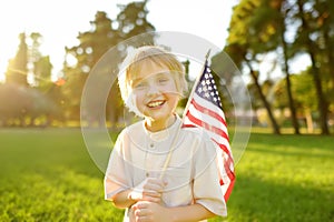 Cute little boy celebrating of July, 4 Independence Day of USA in park at sunny summer sunset. Child holding american flag symbol
