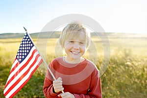 Cute little boy celebrating of July, 4 Independence Day of USA at sunny summer sunset. Child running with american flag of United