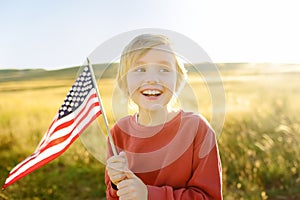 Cute little boy celebrating of July, 4 Independence Day of USA at sunny summer sunset. Child running with american flag of United