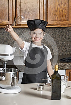 Cute little boy in chef uniform with cooking whisk held high