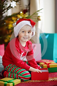 Cute little boy with a Christmas gift under fir tree at home. Portrait of happy kid in Christmas morning