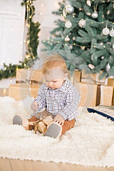 Cute little boy by the Christmas tree and fireplace decorated with garlands and gifts.