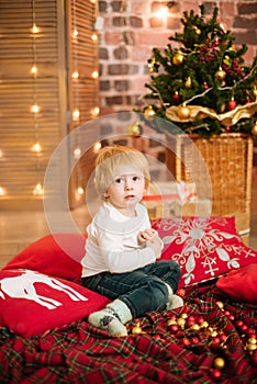 Cute little boy by the Christmas tree and fireplace decorated with garlands and gifts.
