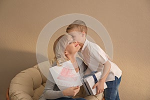 Cute little boy congratulating his mother on color background