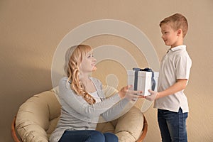 Cute little boy congratulating his mother on color background