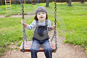 Cute little boy in denim overall swinging on playpit