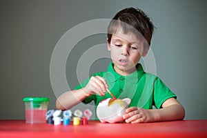 Cute little boy diligently painting his piggy toy photo