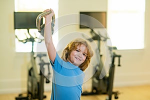 Cute little boy doing exercises with kettlebell. Portrait of sporty child with dumbbells. Child workout kid in gym