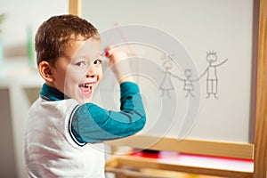 Cute little boy drawing on white board with felt pen and smiling