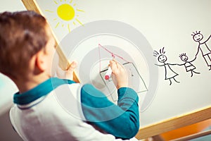 Cute little boy drawing on white board with felt pen and smiling