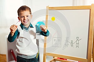 Cute little boy drawing on white board with felt pen and smiling