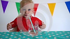 Cute little boy drinking apple juice using straw while sitting at table. Gimbal