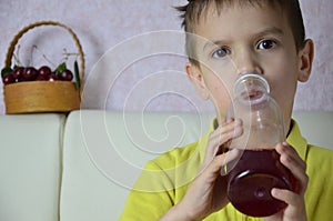 Cute little boy drinking juice at home, cherry juice drinks from a bottle or a glass with a straw.