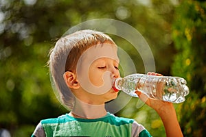 Cute little boy drinking mineral water from the plastic bottle i