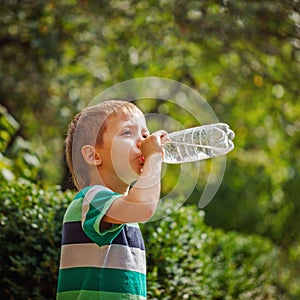 Cute little boy drinking mineral water from the plastic bottle i