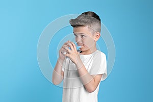 Cute little boy drinking water from glass on light blue background