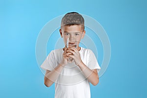 Cute little boy drinking water from glass on light blue background