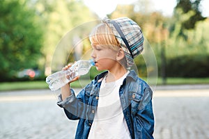 Cute little boy drinking water from the plastic bottle. Child drinks water outdoor