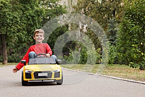 Cute little boy driving children`s car outdoors. Space for text