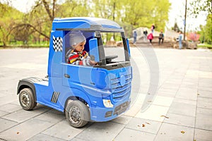 Cute little boy driving electric toy car outdoors in park.