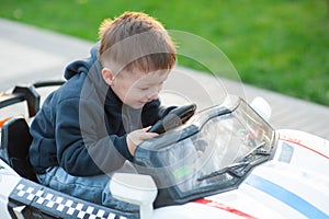 Cute little boy driving mechanical toy car turning the steering wheel with a look of concentration as he plays in a city park