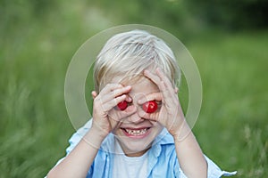 Cute little boy, eating cherry outdoors, making funny faces and playing with cherry, having fun
