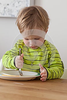 Cute little boy eating in cozy dining room. Child having a dinner at home. Healthy nutrition for small kids.