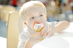 Cute little boy eating ice cream in a waffle cone. Child is tasting gelato in Italian cafe. Unhealthy street fast food