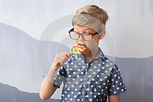 Cute little boy eating lollipop near grey wall