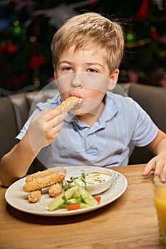 Cute little boy eating nuggets during New Year dinner in restaurant