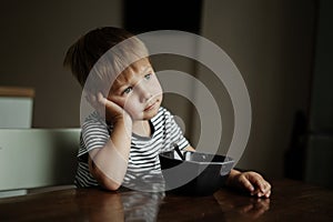 Cute little boy eating oatmeals for beakfast dreamily looking at the window. image with selective focus