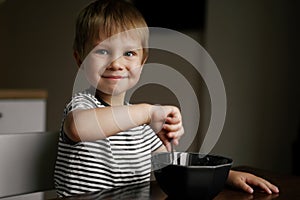 Cute little boy eating oatmeals for beakfast dreamily looking at the window. image with selective focus