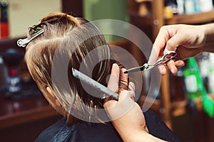 Cute little boy getting haircut by hairdresser at the barbershop. Barber man doing kid the hairstyle