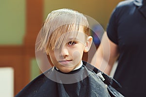 Cute little boy getting haircut by hairdresser at the barbershop. Barber man doing kid the hairstyle