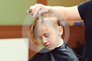 Cute little boy getting haircut by hairdresser at the barbershop. New hairstyle for young boy